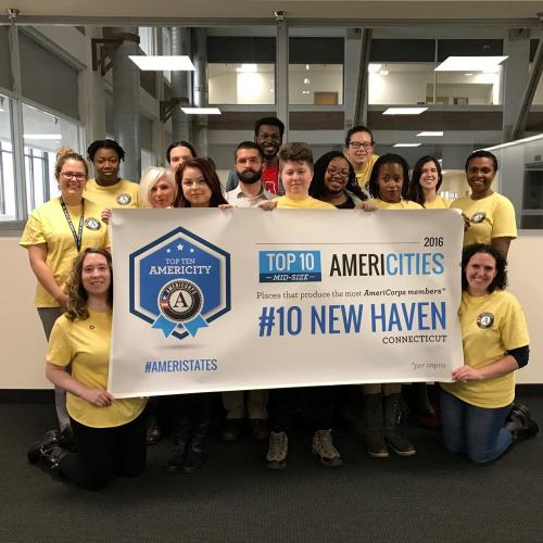 Fifteen people in yellow AmeriCorps shirts hold a sign that reads "Top 10 AmeriCities: #10 New Haven"